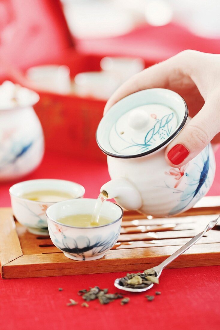 Frau giesst Grüntee aus Teekanne in asiatische Teeschälchen (Asien)