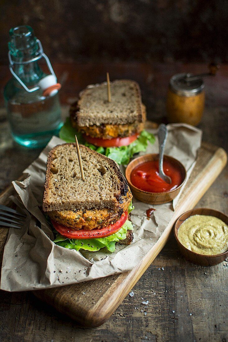 Sandwich mit veganer Frikadelle, Tomaten, Salat, Senf und Ketchup