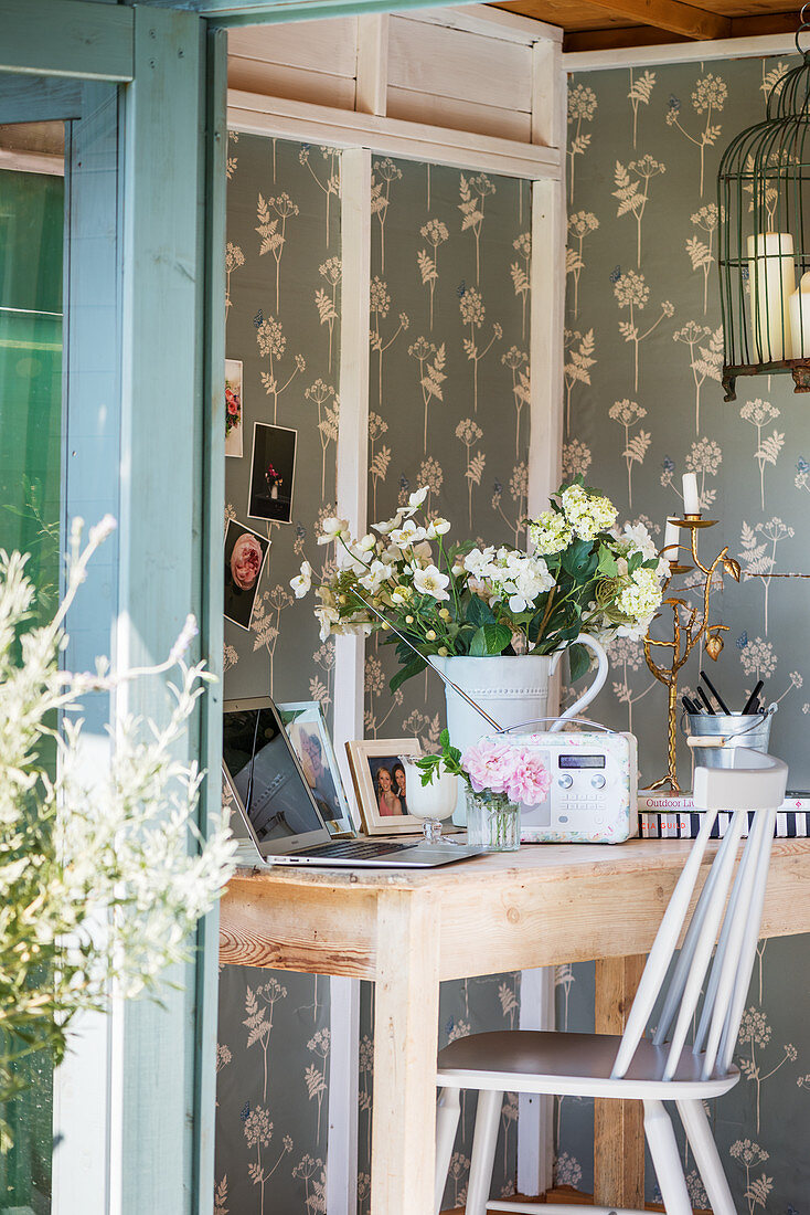 White flowers, retro radio and laptop on wooden table in summerhouse