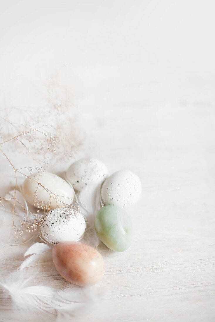 Easter eggs and feathers on white wooden surface