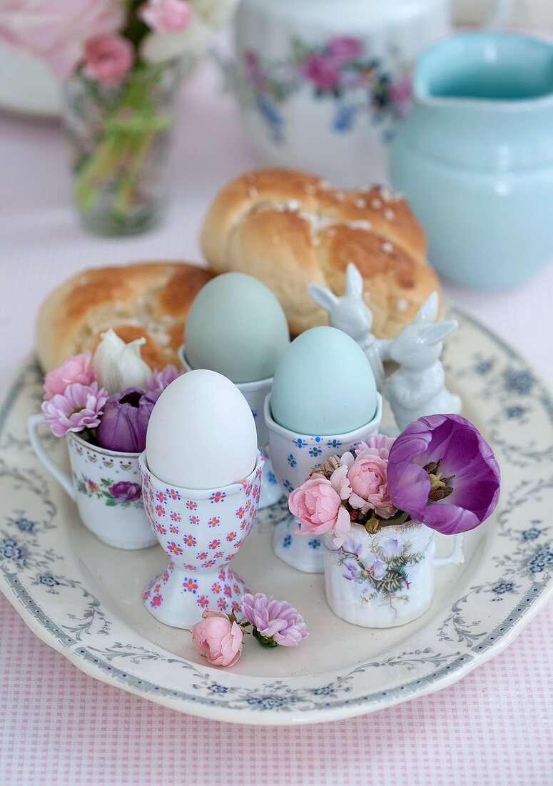 Eggs in egg cups, flowers in cups and pastries on Easter table