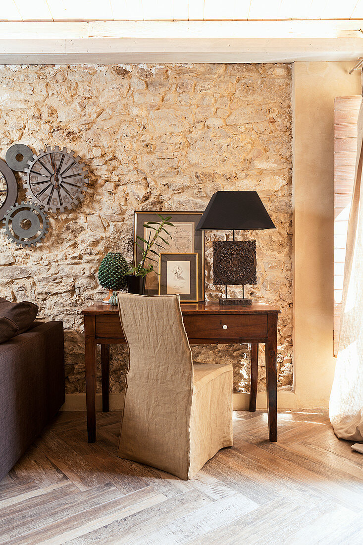 Desk and loose-covered chair in front of stone wall in living room