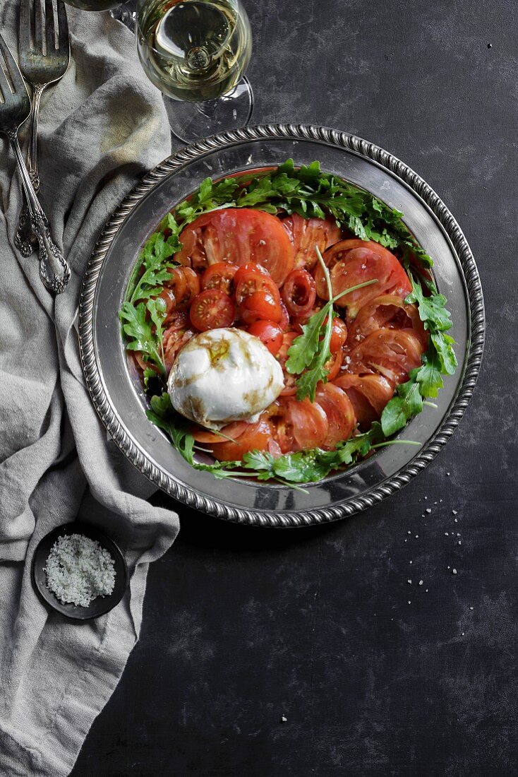 Caprese-Salat mit Tomaten, Mozzarella und Rucola auf silberner Servierplatte