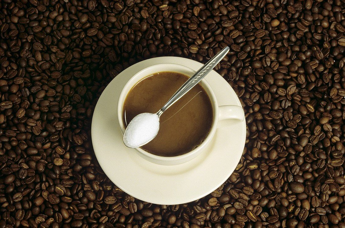 Cup of coffee with milk & spoon with sugar on coffee beans