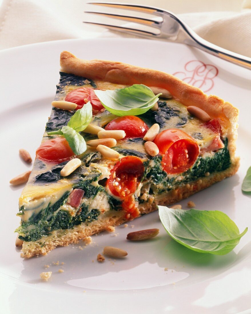 A piece of spinach & tomato quiche with pine nuts & basil