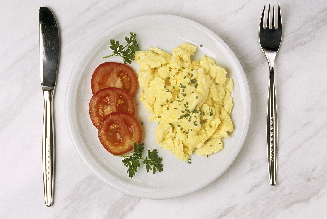 Scrambled egg with parsley on plate with tomato slices