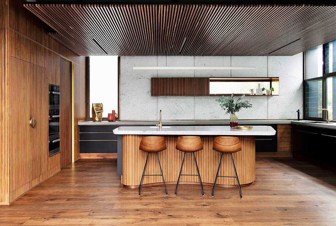 Kücheninsel mit Marmorplatte und Barhockern in offener Küche mit Holzverkleidung