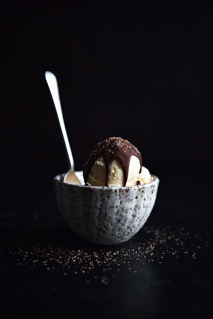 Vanilleeis mit Schokoladensauce im Schälchen vor schwarzem Hintergrund
