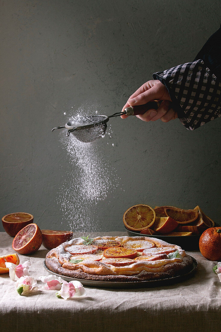 Hand sprinkling sugar powder homemade Cheesecake with sicilian blood oranges, decorated by edible flowers