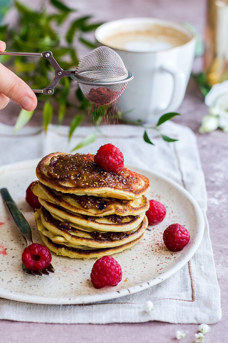 Gestapelte Pancakes mit Himbeeren, Feigenmarmelade und Erdbeerpulver, dazu Kaffee