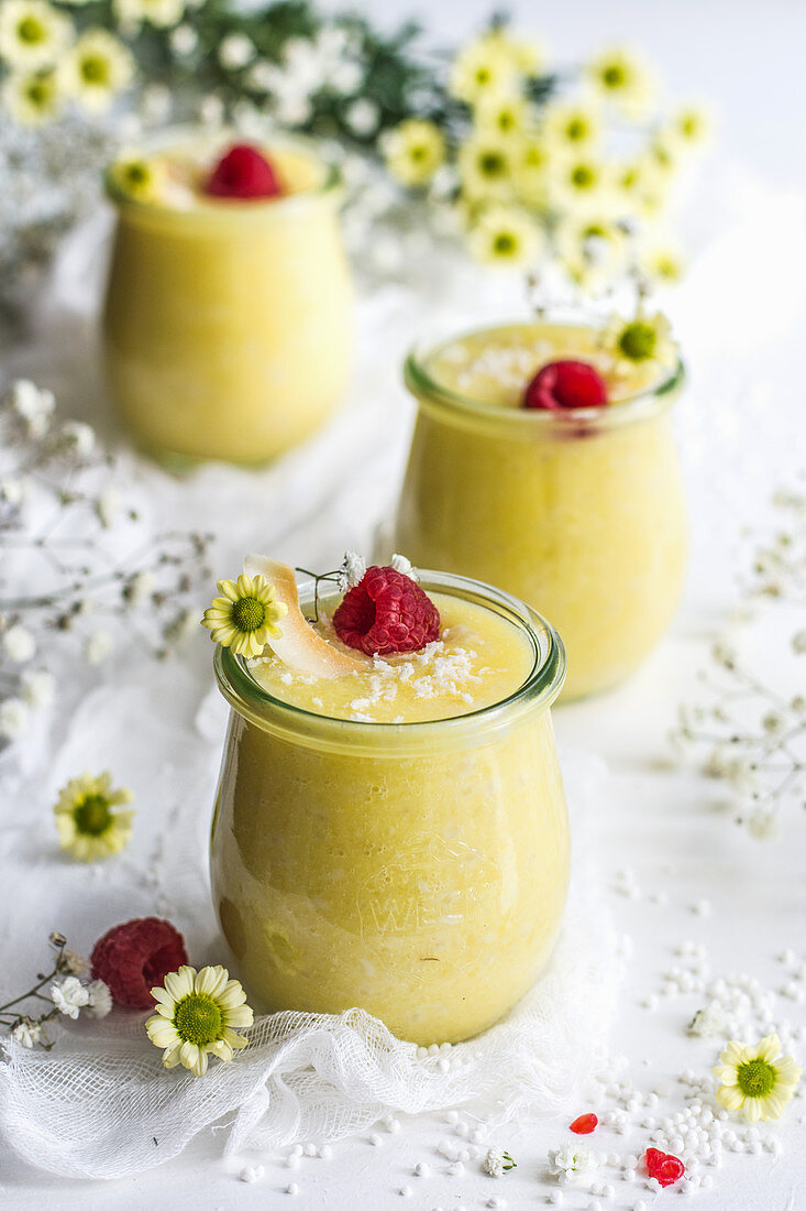 Coconut and pineapple tapioca dessert served in jars with raspberries and coconut flakes