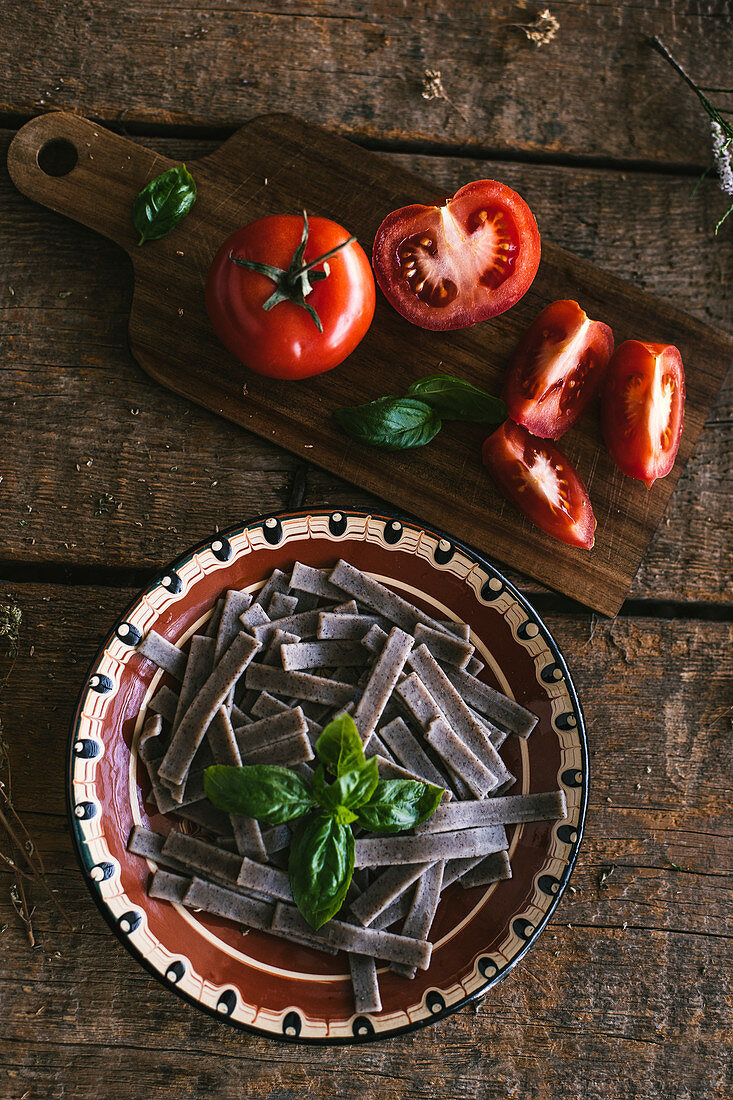 Buckwheat pasta with basil and tomato on a wooden table