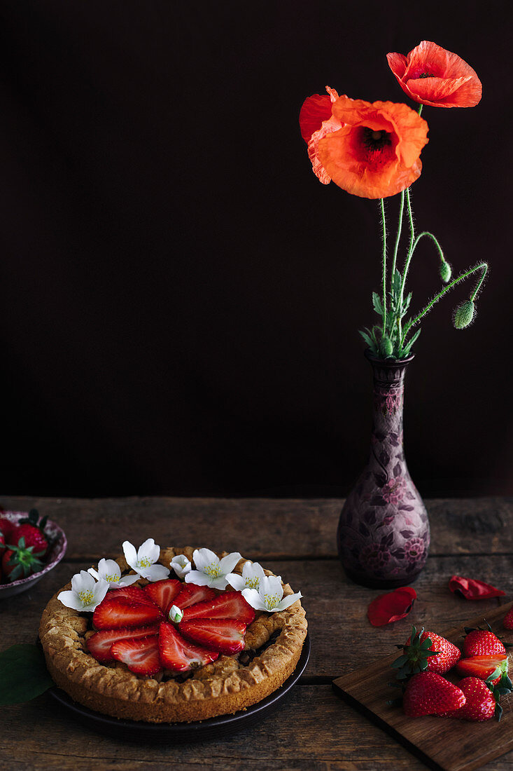 Mini-Erdbeertarte auf Holztisch daneben Mohnblume in Vase