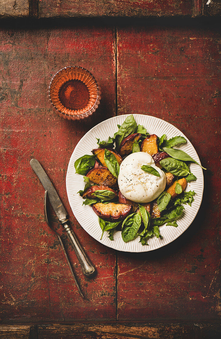Flat-lay of seasonal salad with Burrata soft cheese and grilled peaches with glass of rose wine