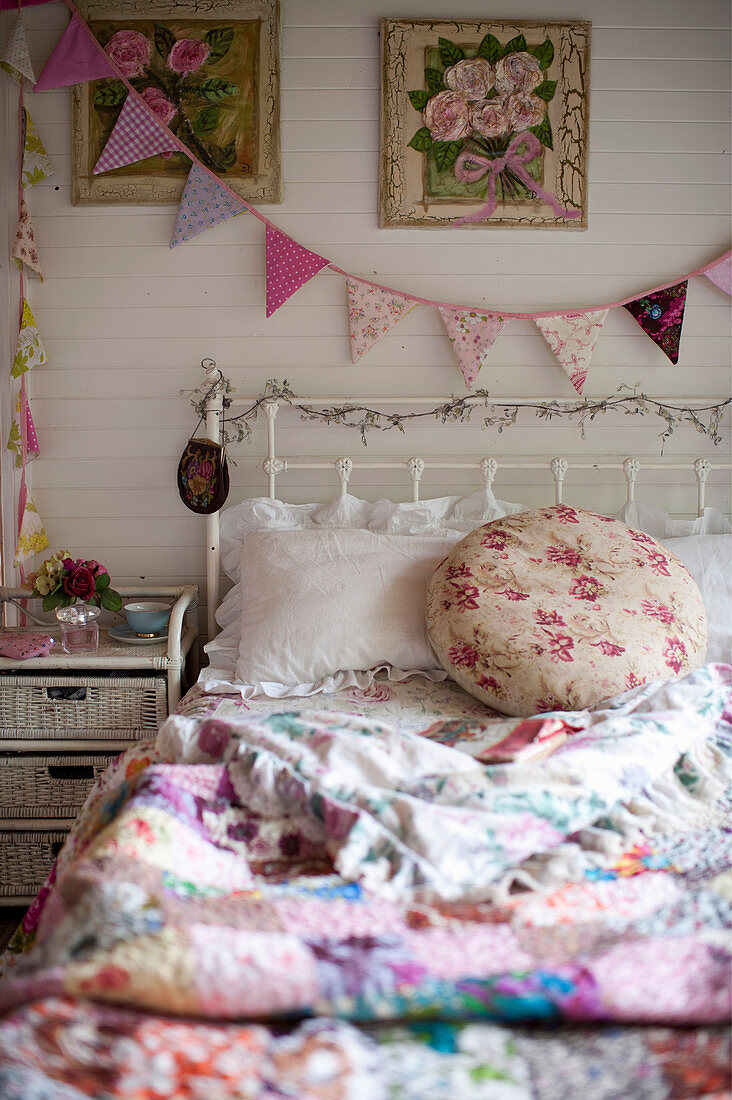 Old bed with colourful, vintage-style bed linen and rattan bedside table below bunting on wall