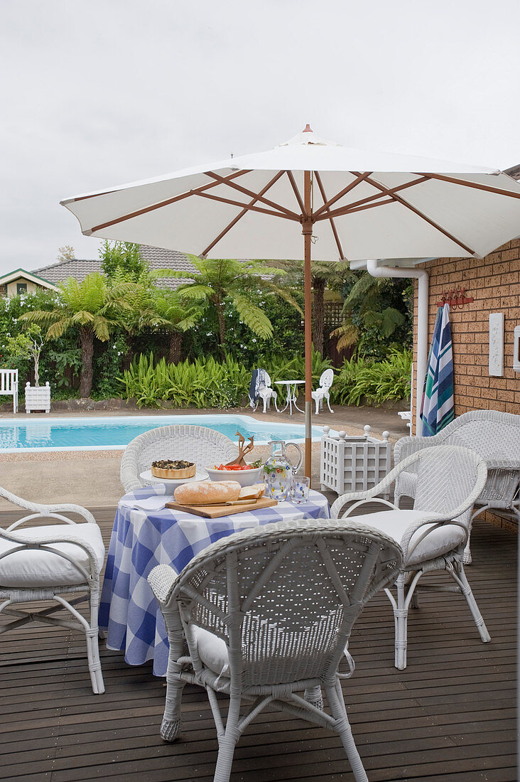 Bistro table with checked tablecloth and wicker chairs below parasol on wooden deck