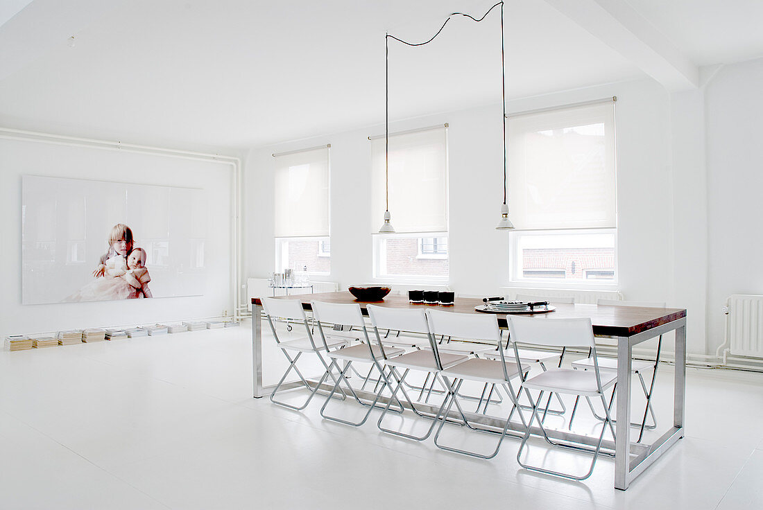 Folding chairs around long table in minimalist dining room with white floor