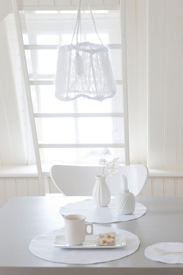 Place setting on dining table below pendant lamp in white interior