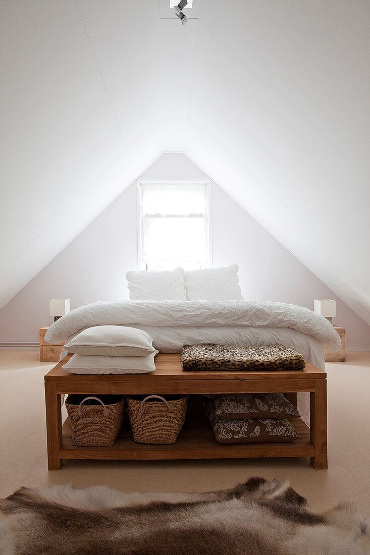 Wooden bench at foot of bed in white attic bedroom