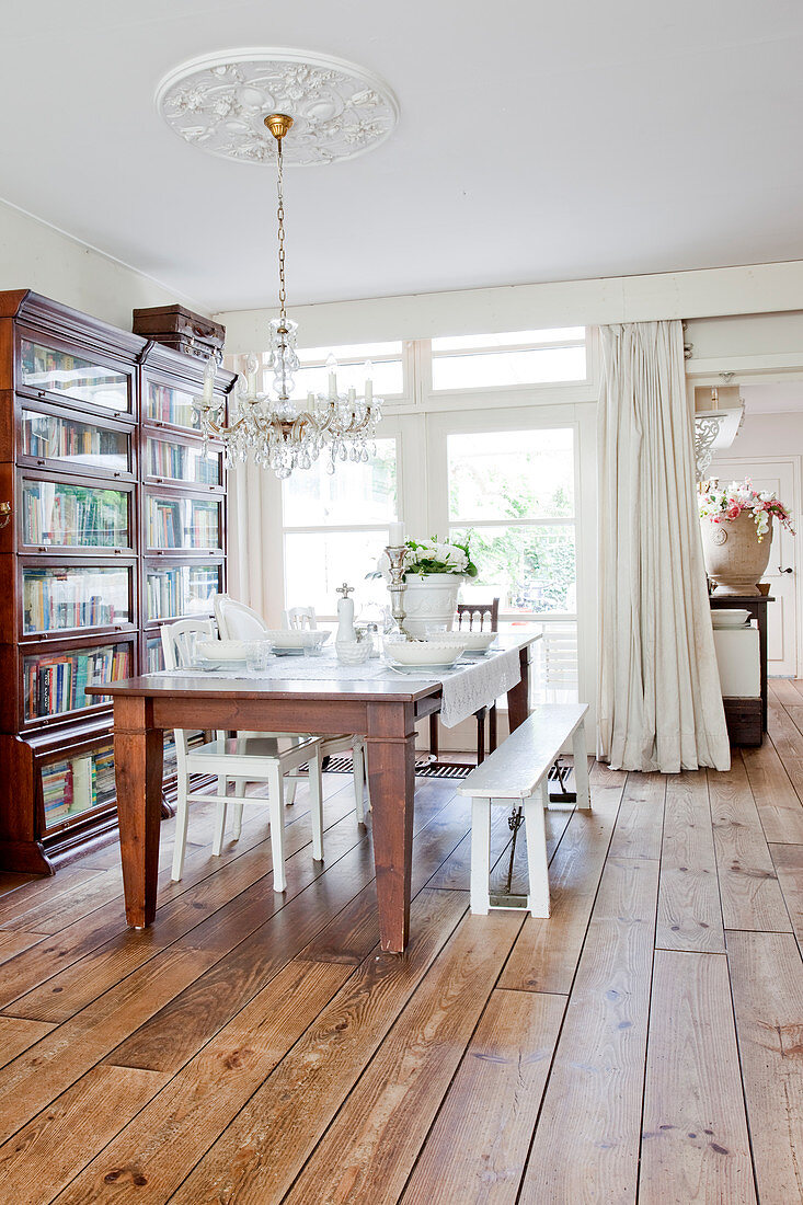 Rustic wooden table set in white below chandelier in dining area