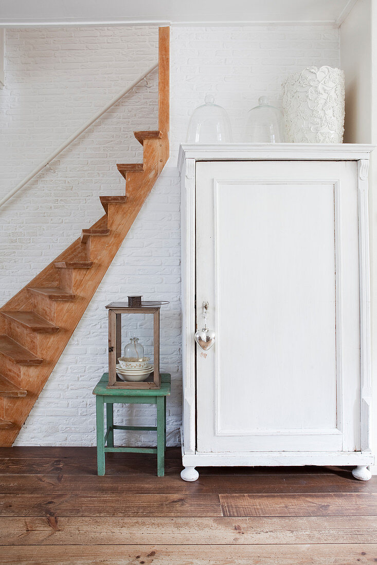 White cupboard in hallway next to wooden staircase