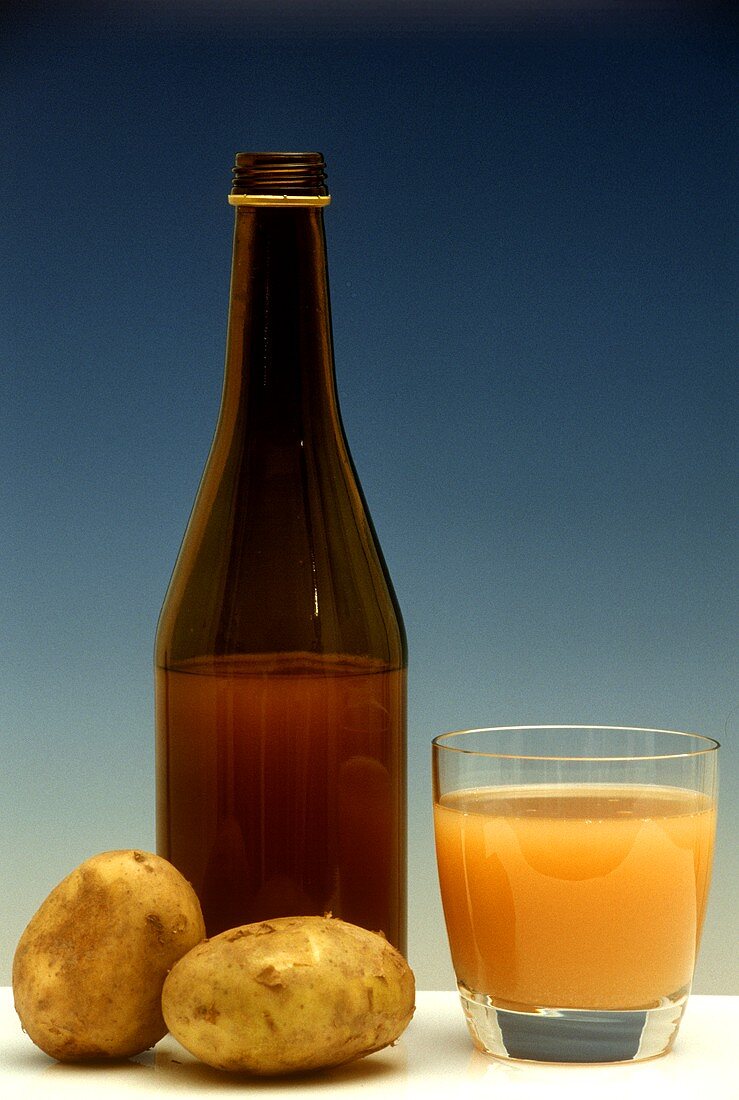 Potato juice in glass and bottle and two potatoes