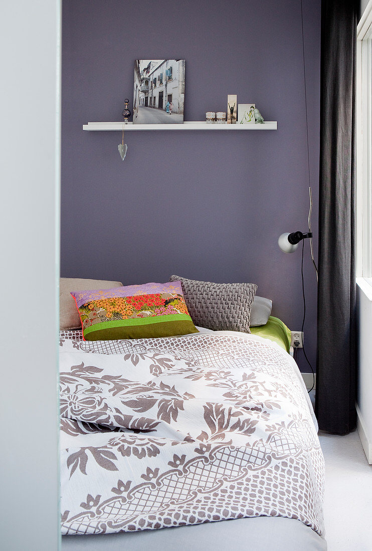 Double bed with bedspread and colourful scatter cushions against purple bedroom wall