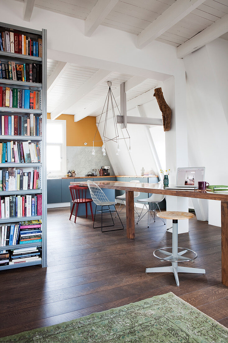 Long dining table with various chairs and bookcase in open-plan interior