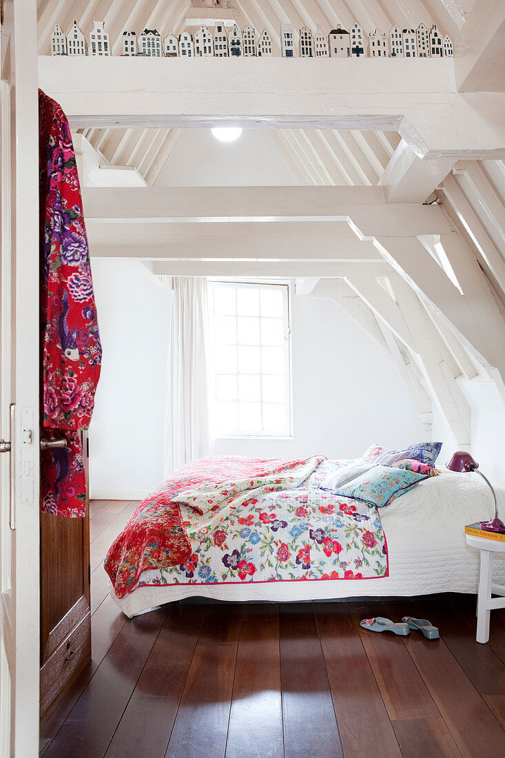 Colourful scatter cushions and quilt on double bed in white attic room