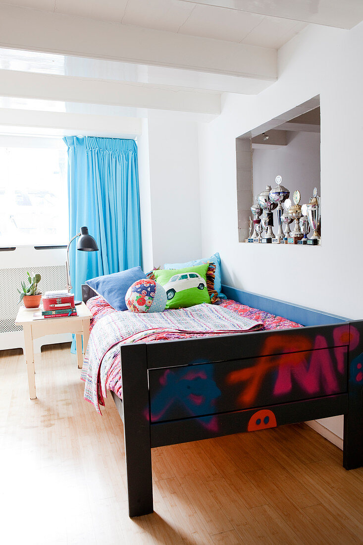 Holzbett mit bunten Decken und Pokale in Wandnische im Jungenzimmer mit türkisblauem Vorhang