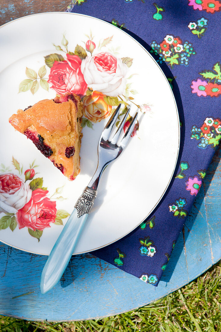A piece of berry cake on a plate with a floral printed napkin