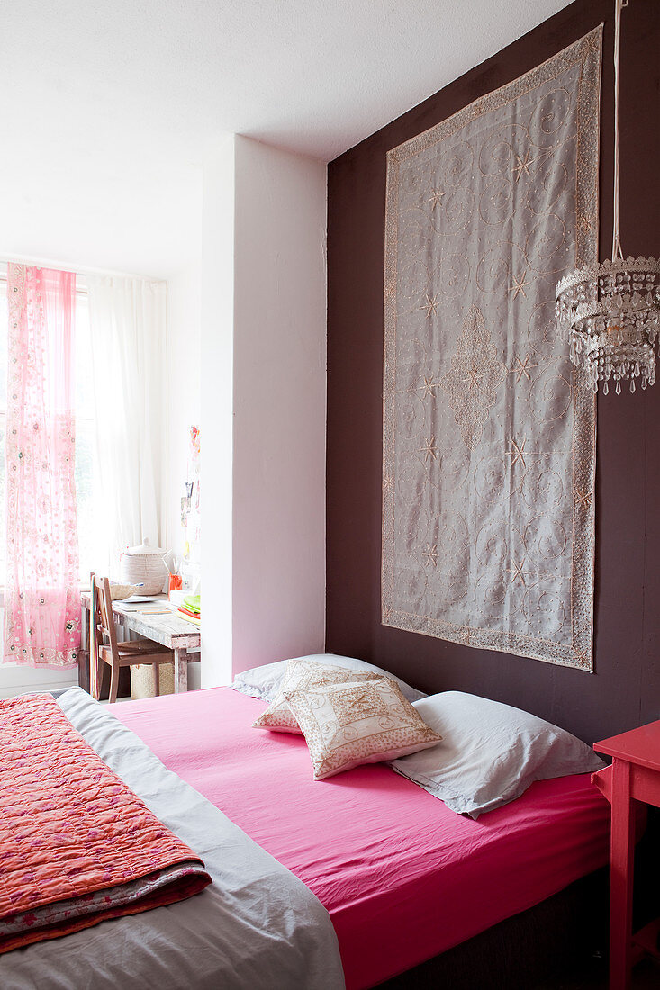 Mattress with a pink sheet in front of a dark wall with a tapestry in the bedroom