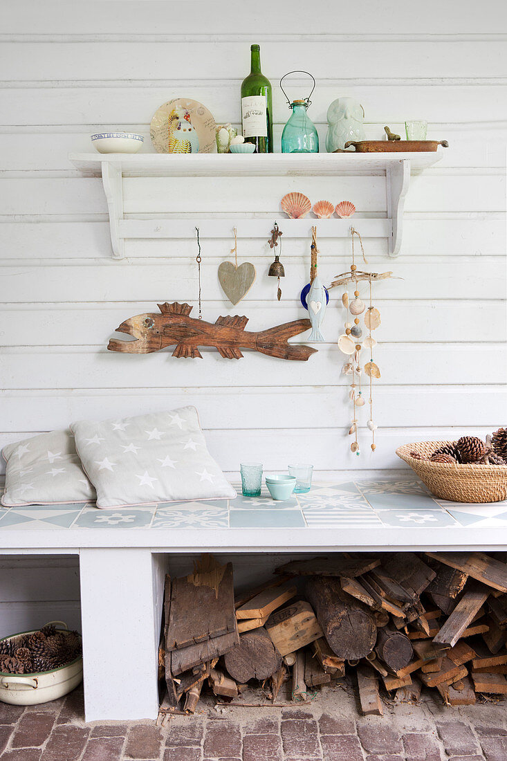 Maritime ornaments on shelf on board wall above bench with firewood stored below