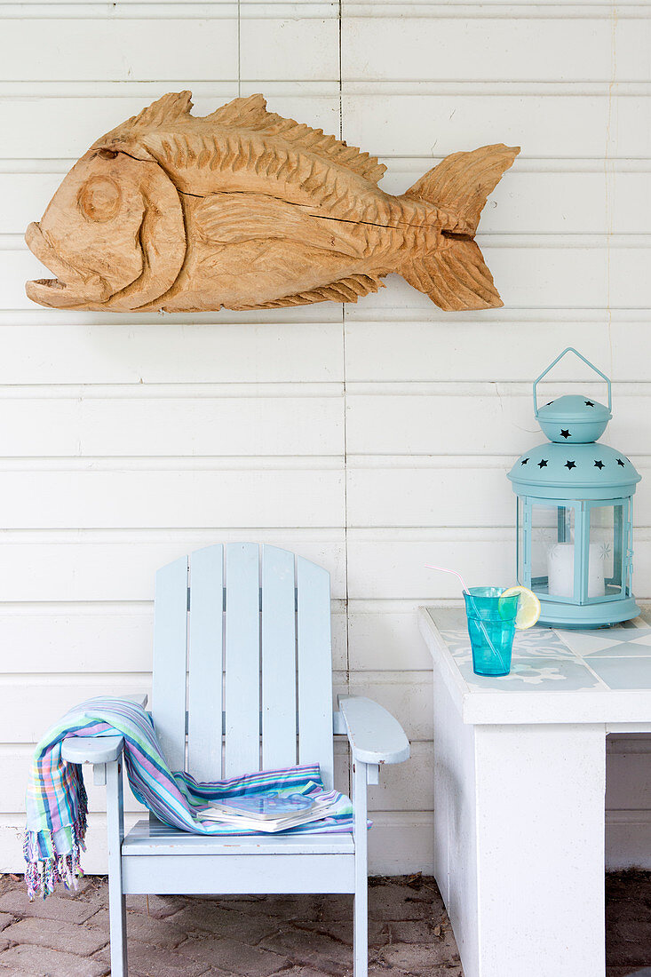Wooden sculpture of fish on board wall above pale blue deckchair