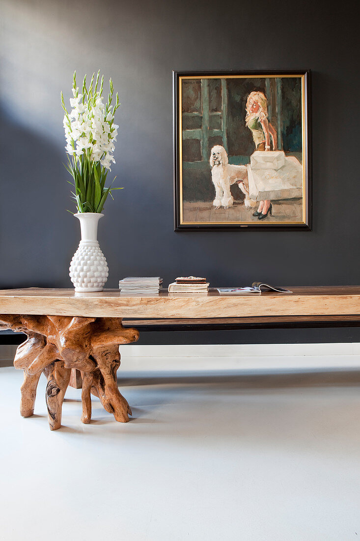 Rustic table with legs made from polished tree roots below painting on grey wall