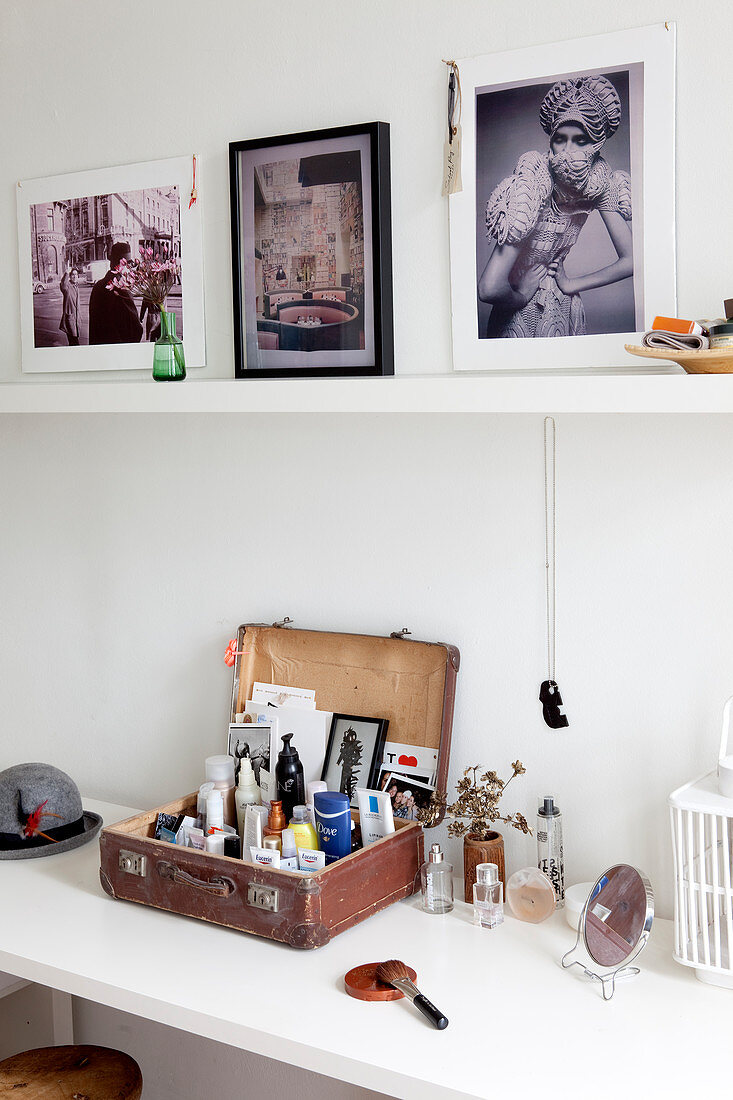 Vintage suitcase of cosmetics on dressing table below photographs on shelf