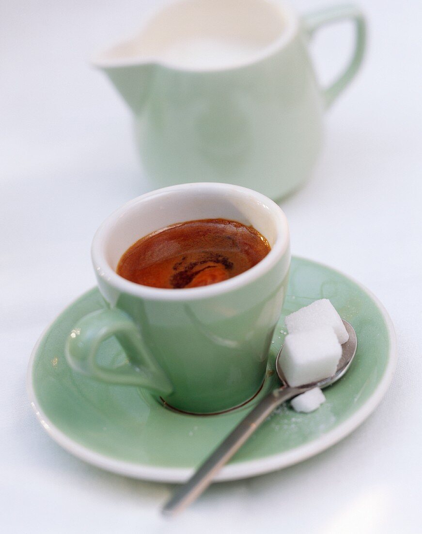Espresso in grüner Tasse, Löffel, Würfelzucker, Milchkännchen