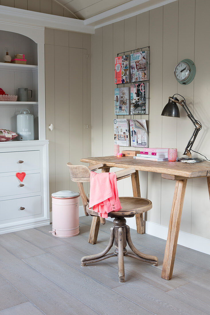 Old swivel chair in front of a rustic wooden desk in front of a wood paneled wall