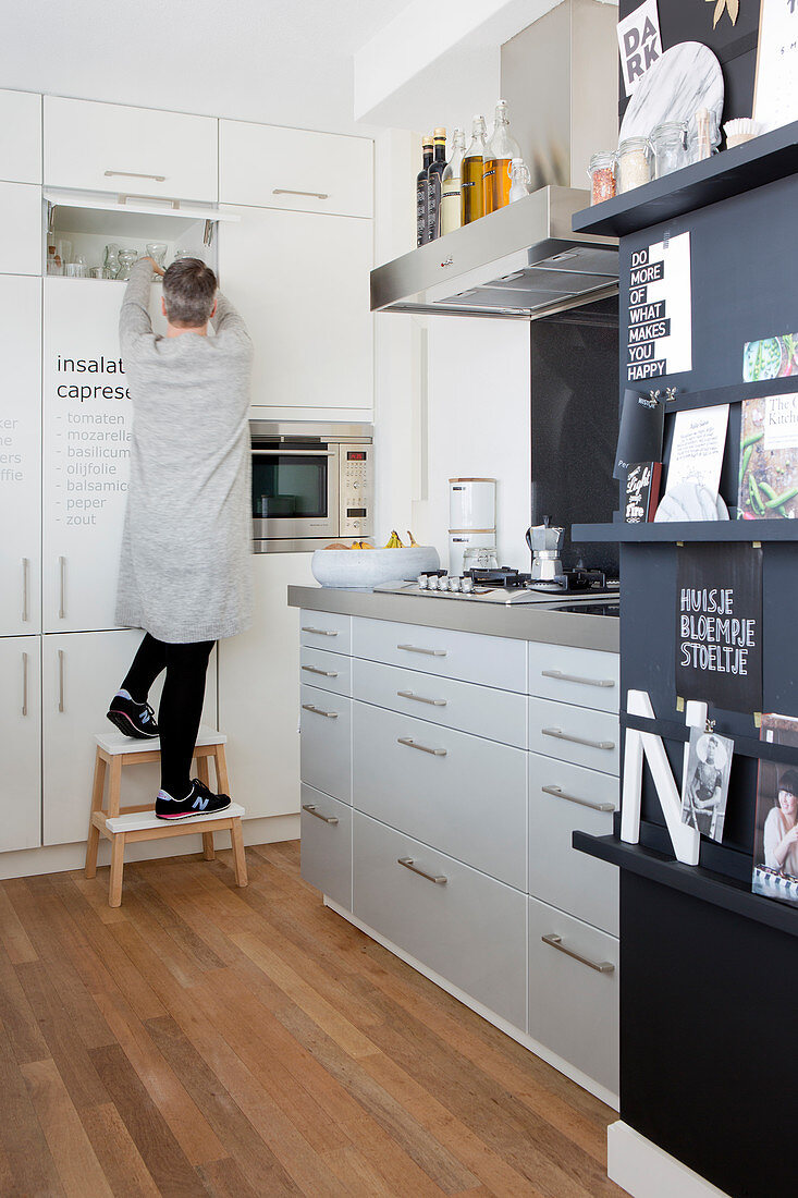 Woman opening white, floor-to-ceiling cupboards in kitchen