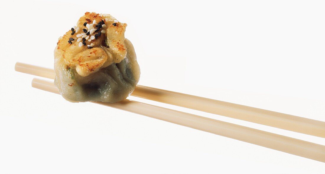 Chopsticks holding dim sum, filled with black cumin & sesame