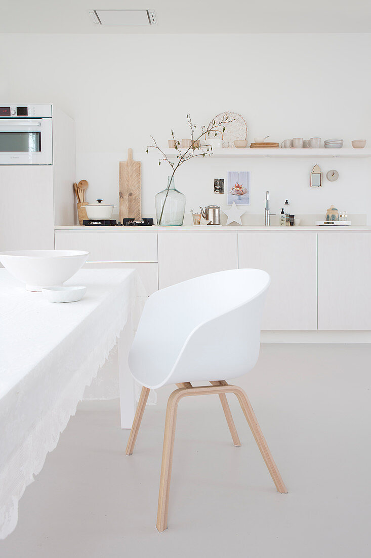 White shell chair at table with white tablecloth in kitchen-dining room with white kitchen counter
