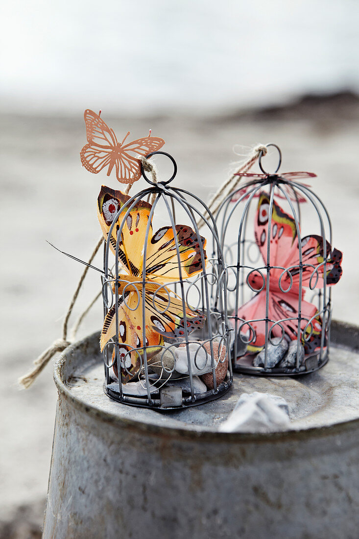 Schmetterlinge aus Federn und Metall in kleinen Deko-Käfigen