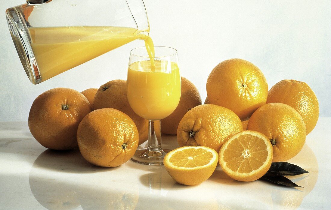 Orangensaft wird ins Glas gegossen, Deko: frische Orangen