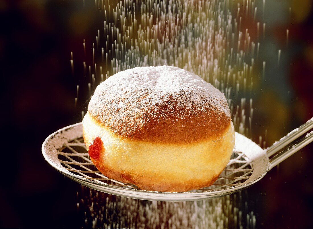 A fritter on scoop being sprinkled with icing sugar