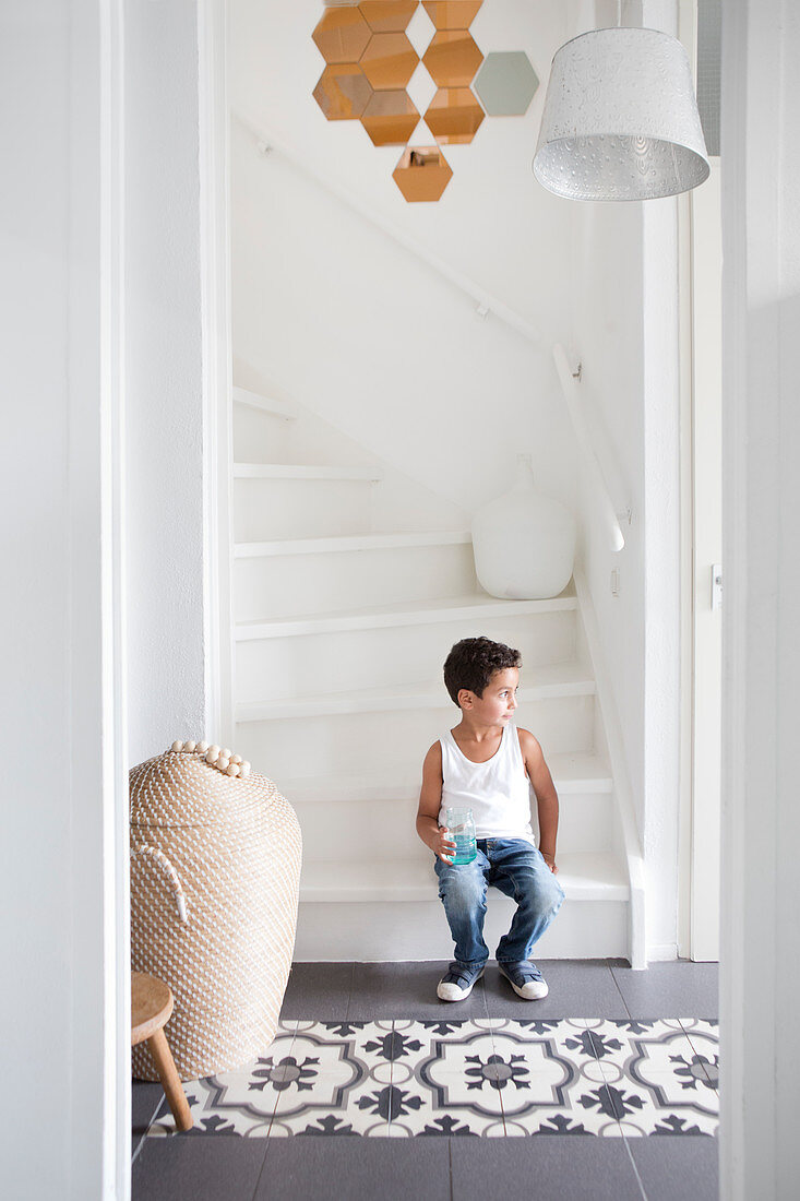 Boy sitting on white stairs in a hallway with patterned tiles