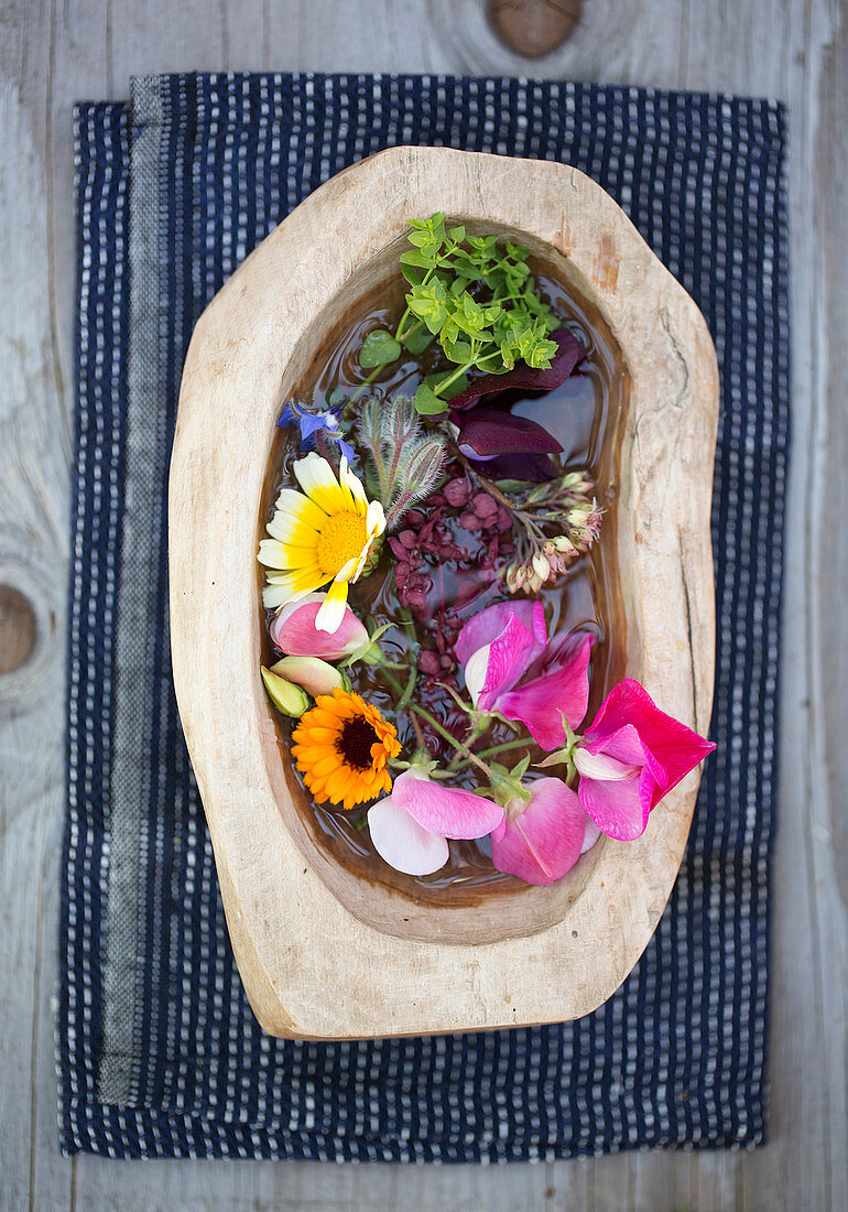 Sweet pea, marigold, chrysanthemum, and borage in a wooden bowl with water