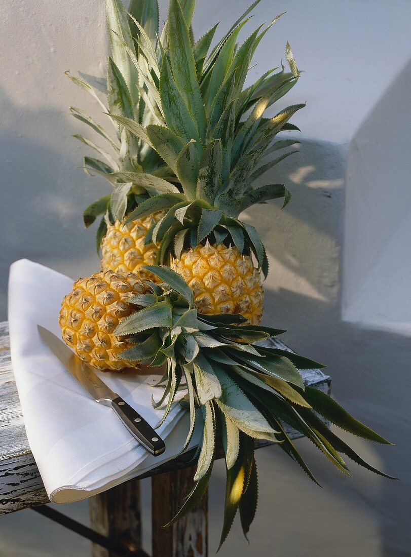 Drei Ananas & ein Messer auf Tuch auf Holztisch