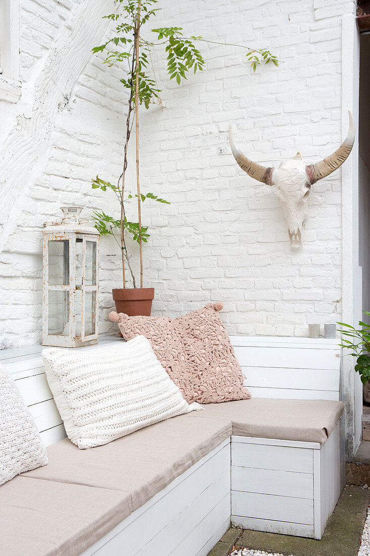 Wooden bench with pillows and antlers on a terrace with whitewashed brick wall
