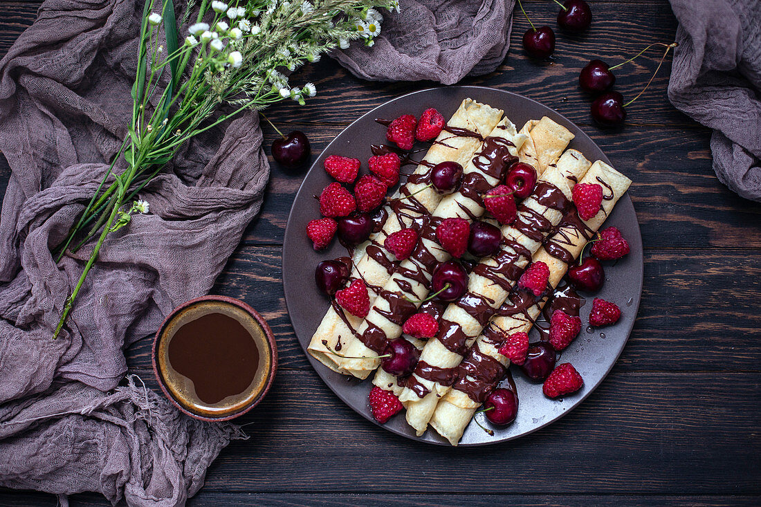 Crepes drizzled with chocolate and topped with fresh cherries and raspberries