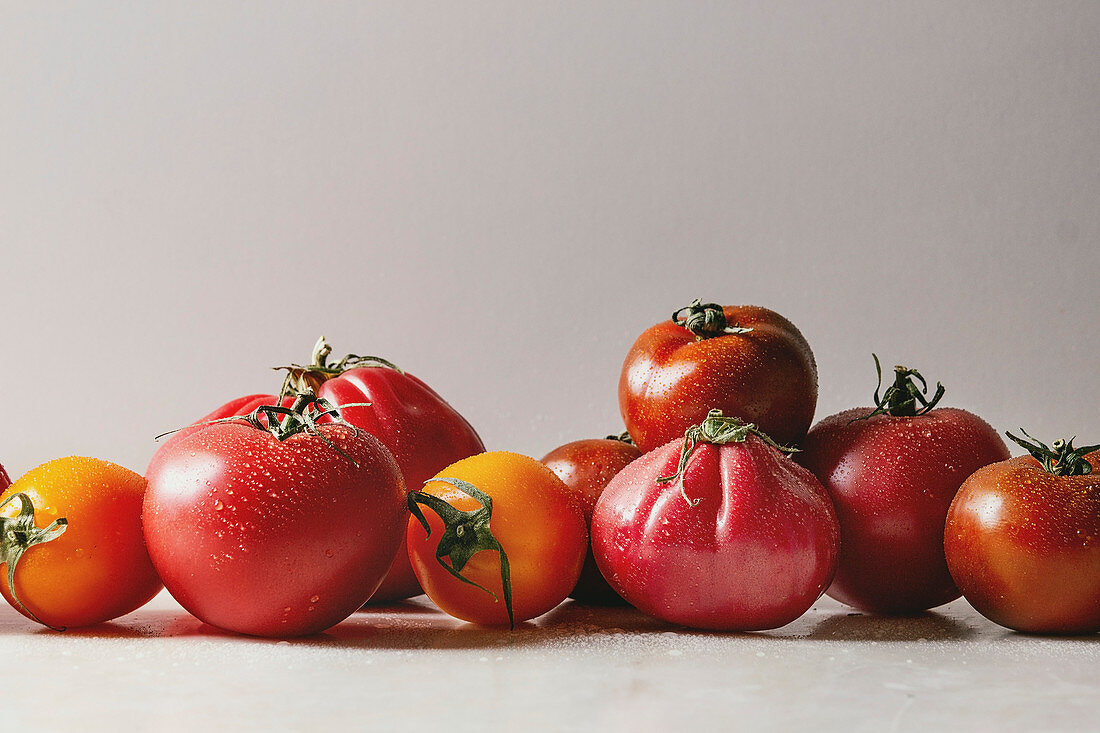 Variety of ripe fresh organic gardening tomatoes on white marble table